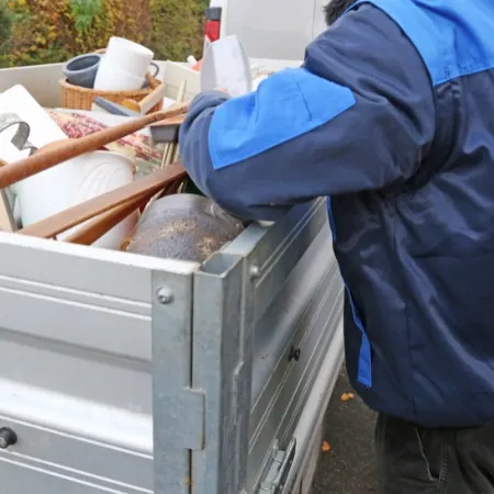 Person lädt Hausrat in einen offenen Metallcontainer