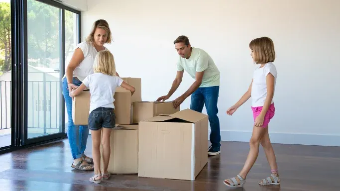 Familie trägt Umzugskartons in eine helle, frisch bezogene Wohnung
